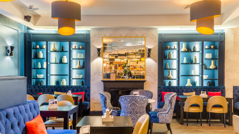 A comfortable lounge with blue decor and red accents. A cosy fireplace in the centre.